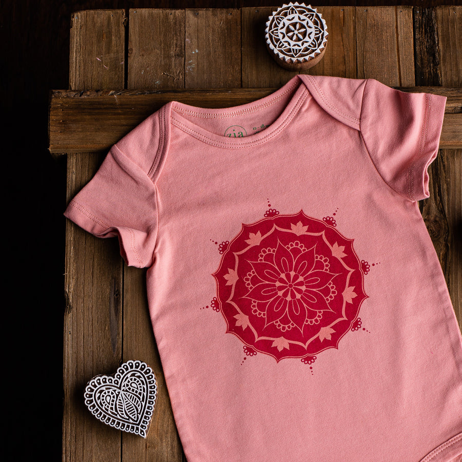 Pink short sleeve baby onesie with mandala print on wooden background