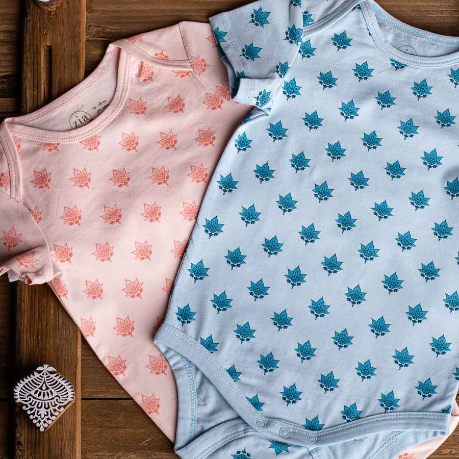 Two short sleeve baby onesies in pink and blue with lotus flower print