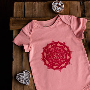Pink short sleeve baby onesie with mandala print on wooden background