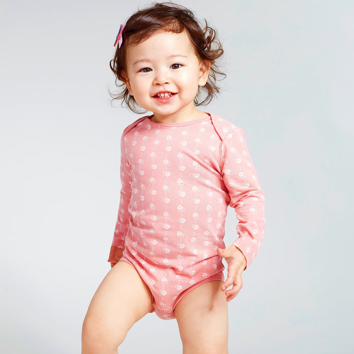 Happy baby girl wearing a pink long sleeve baby onesie with heart print
