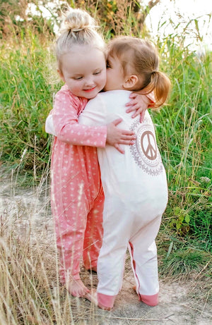 Two baby girls wearing one piece rompers and hugging each other